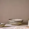 Malia stoneware collection by Nkuku, showing the cream bowl alongside matching plates, mugs, jugs and serving pieces with soft reactive glaze and hand-painted line detail.