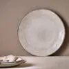 Malia Dinner Plate - Cream by Nkuku, a 28cm cream stoneware dinner plate with a shallow rounded shape, soft reactive glaze and hand-painted rim detail.