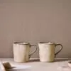 Malia Mug - Cream Set of 2 by Nkuku styled for tea or coffee, showing the rounded mug shape, warm cream glaze and relaxed stoneware finish.