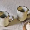 Close-up of the Malia Mug - Cream by Nkuku, showing the cream stoneware surface, textured handle, subtle glaze variation and fine hand-painted line detail.