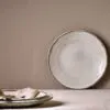 Malia Side Plate - Cream by Nkuku, a 22.5cm cream stoneware side plate with a shallow organic shape, soft reactive glaze and hand-painted rim detail.