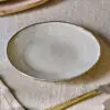 Malia Side Plate - Cream by Nkuku, a 22.5cm cream stoneware side plate with a shallow organic shape, soft reactive glaze and hand-painted rim detail.