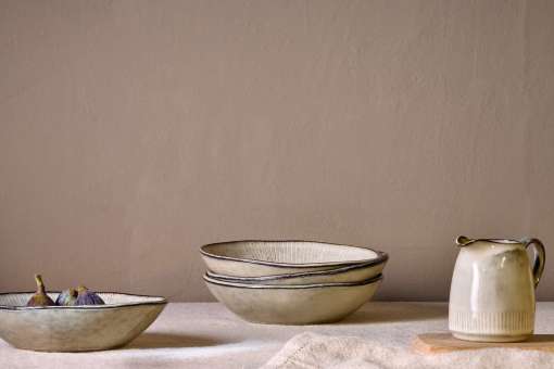 Malia stoneware collection by Nkuku, showing the cream bowl alongside matching plates, mugs, jugs and serving pieces with soft reactive glaze and hand-painted line detail.