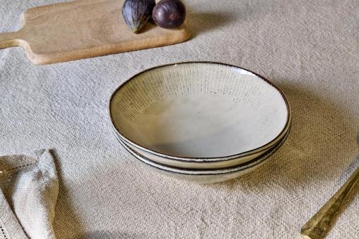 Malia Bowl - Cream by Nkuku, a 615ml cream stoneware bowl with a low rounded shape, soft reactive glaze and hand-painted line detail around the rim.