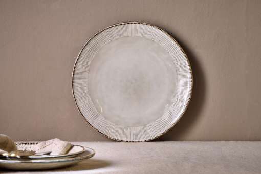 Malia stoneware collection by Nkuku, showing the cream dinner plate alongside matching bowls, mugs, jugs and serving pieces with soft reactive glaze and hand-painted line detail.