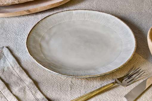 Malia stoneware collection by Nkuku, showing the cream dinner plate alongside matching bowls, mugs, jugs and serving pieces with soft reactive glaze and hand-painted line detail.