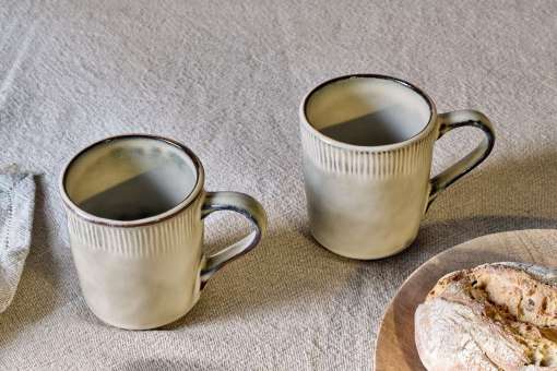 Close-up of the Malia Mug - Cream by Nkuku, showing the cream stoneware surface, textured handle, subtle glaze variation and fine hand-painted line detail.