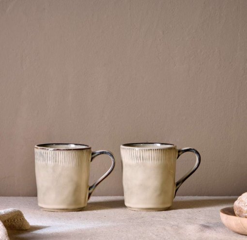 Malia Mug - Cream Set of 2 by Nkuku, showing two 380ml cream stoneware mugs with organic shapes, soft reactive glaze and hand-painted rim detail.