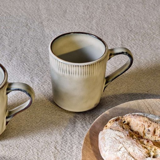 Malia Mug - Cream Set of 2 by Nkuku, showing two 380ml cream stoneware mugs with organic shapes, soft reactive glaze and hand-painted rim detail.