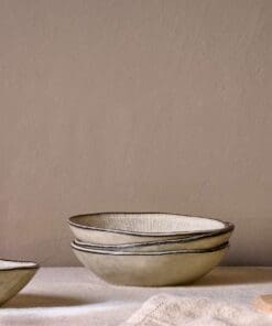 Malia stoneware collection by Nkuku, showing the cream bowl alongside matching plates, mugs, jugs and serving pieces with soft reactive glaze and hand-painted line detail.