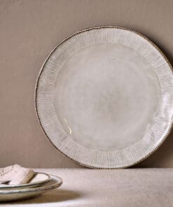 Malia Dinner Plate - Cream by Nkuku, a 28cm cream stoneware dinner plate with a shallow rounded shape, soft reactive glaze and hand-painted rim detail.