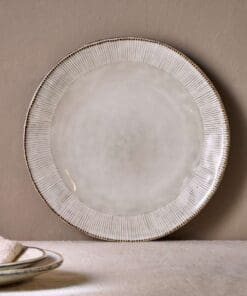 Malia stoneware collection by Nkuku, showing the cream dinner plate alongside matching bowls, mugs, jugs and serving pieces with soft reactive glaze and hand-painted line detail.