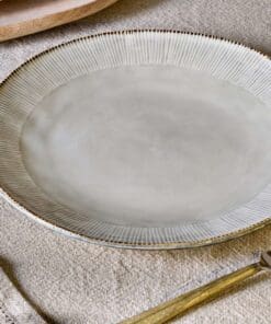 Malia stoneware collection by Nkuku, showing the cream dinner plate alongside matching bowls, mugs, jugs and serving pieces with soft reactive glaze and hand-painted line detail.