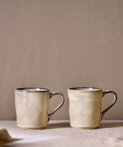 Malia Mug - Cream Set of 2 by Nkuku styled for tea or coffee, showing the rounded mug shape, warm cream glaze and relaxed stoneware finish.