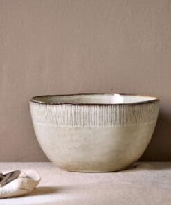 Malia Serving Bowl - Cream by Nkuku styled on a table, showing the generous serving bowl shape, cream glazed finish and relaxed stoneware tableware setting.
