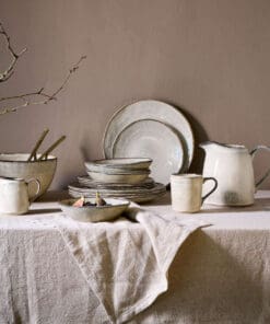 Malia stoneware collection by Nkuku, showing coordinated cream plates, bowls and serving jugs with a soft reactive glaze, fine hand-painted line detail and relaxed organic shapes, styled as a rustic tableware range.