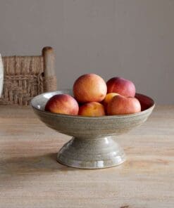 Valinha Earthenware Footed Bowl - Grey by Nkuku styled on a table, showing the raised footed base, shallow serving shape and rustic grey earthenware finish.