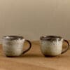 Cam Coffee Mug - Mocha Set of 2 by Nkuku, showing the paired 350ml ceramic mugs with individual glaze variations and rustic tableware style.