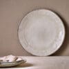 Malia Dinner Plate - Cream by Nkuku, a 28cm cream stoneware dinner plate with a shallow rounded shape, soft reactive glaze and hand-painted rim detail.