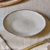 Malia Side Plate - Cream by Nkuku, a 22.5cm cream stoneware side plate with a shallow organic shape, soft reactive glaze and hand-painted rim detail.
