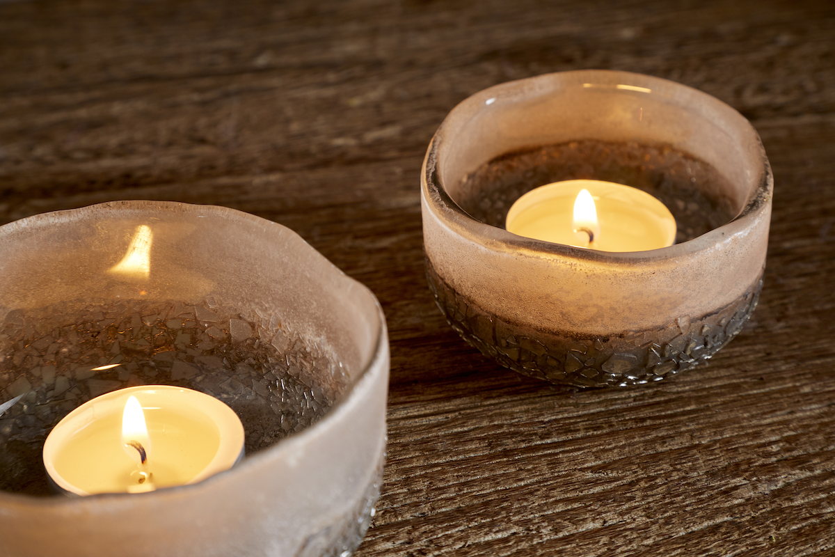 Close Up Riyara Recycled Glass Tealights in Silver Sparkle by Nkuku lit with candles, creating a soft warm glow through the textured glass.