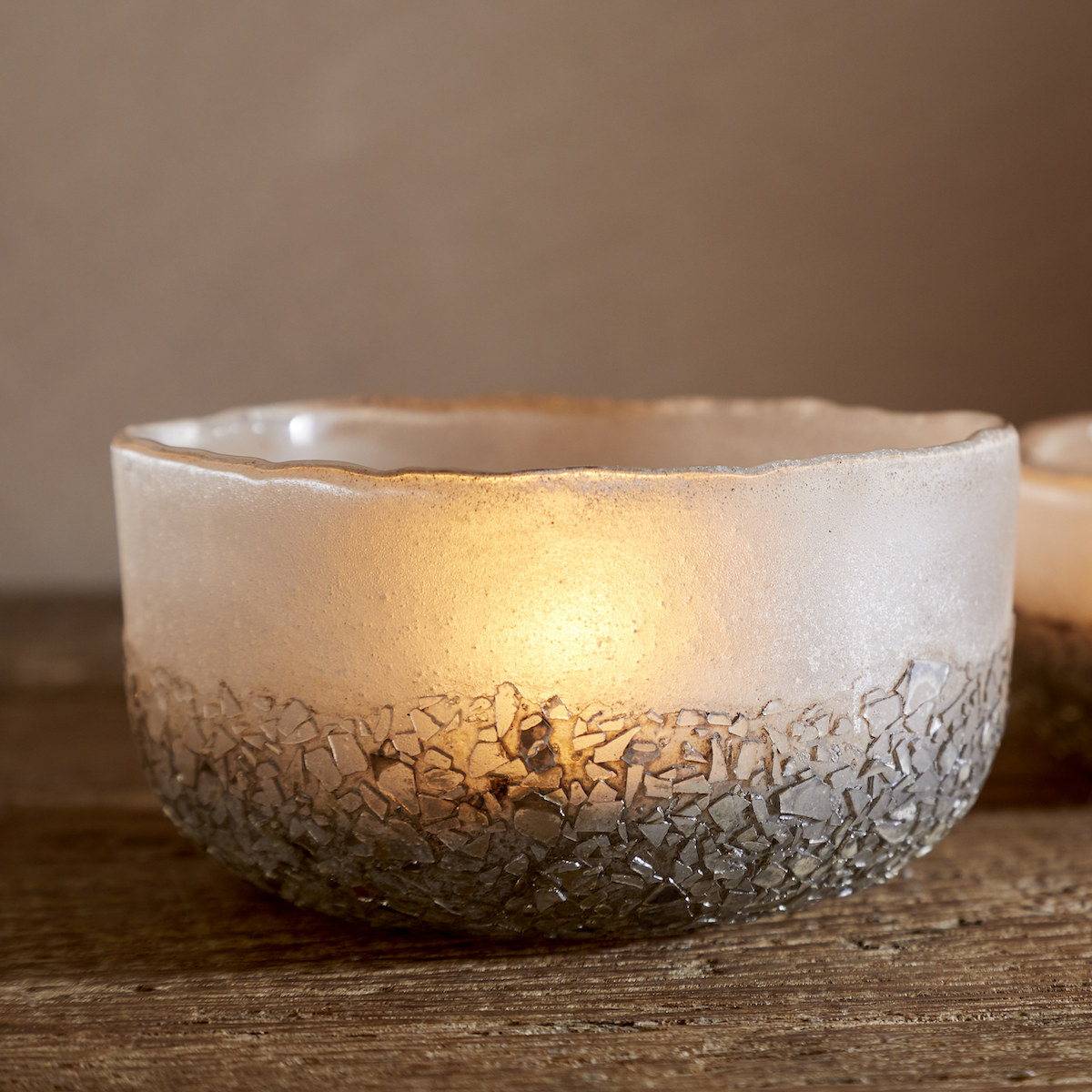 Close up of Riyara Recycled Glass Tealights in Silver Sparkle by Nkuku lit with candles, creating a soft warm glow through the textured glass.