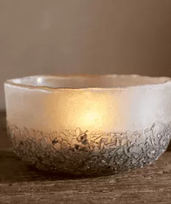 Close up of Riyara Recycled Glass Tealights in Silver Sparkle by Nkuku lit with candles, creating a soft warm glow through the textured glass.