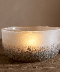 Close up of Riyara Recycled Glass Tealights in Silver Sparkle by Nkuku lit with candles, creating a soft warm glow through the textured glass.