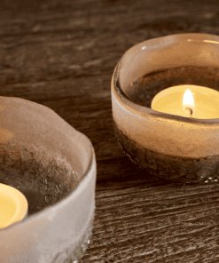 Close Up Riyara Recycled Glass Tealights in Silver Sparkle by Nkuku lit with candles, creating a soft warm glow through the textured glass.
