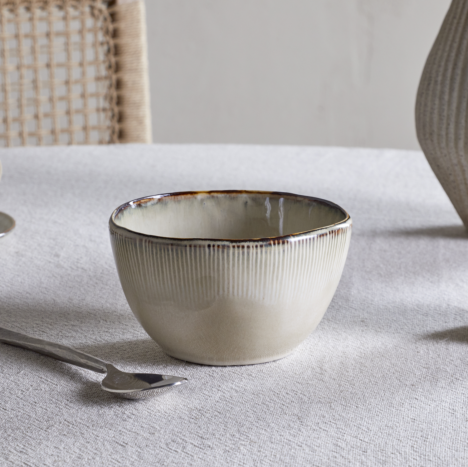 Nkuku Malia Breakfast Bowl in Cream, featuring a softly curved shape, fine vertical ribbed detailing, a warm cream glaze and a contrasting hand-finished brown rim.
